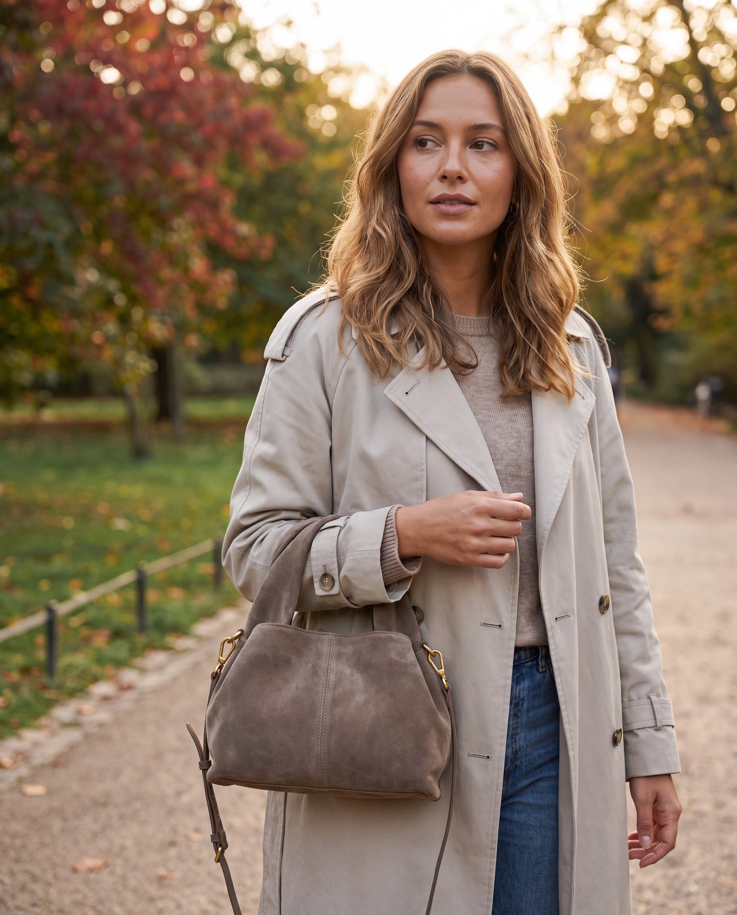 Woman walking a park path in early autumn carrying the Taupe Noemi Suede Handbag