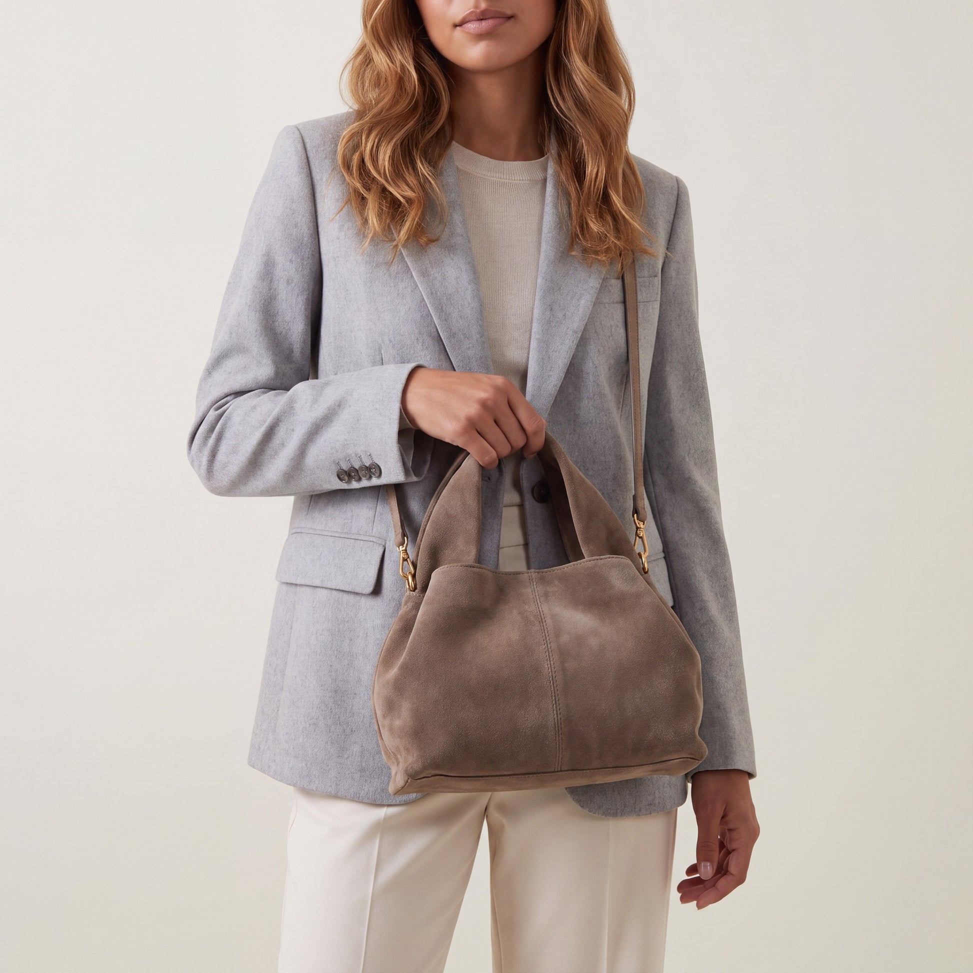 Model holding the Taupe Noemi Suede Handbag in one hand at hip height, studio shot