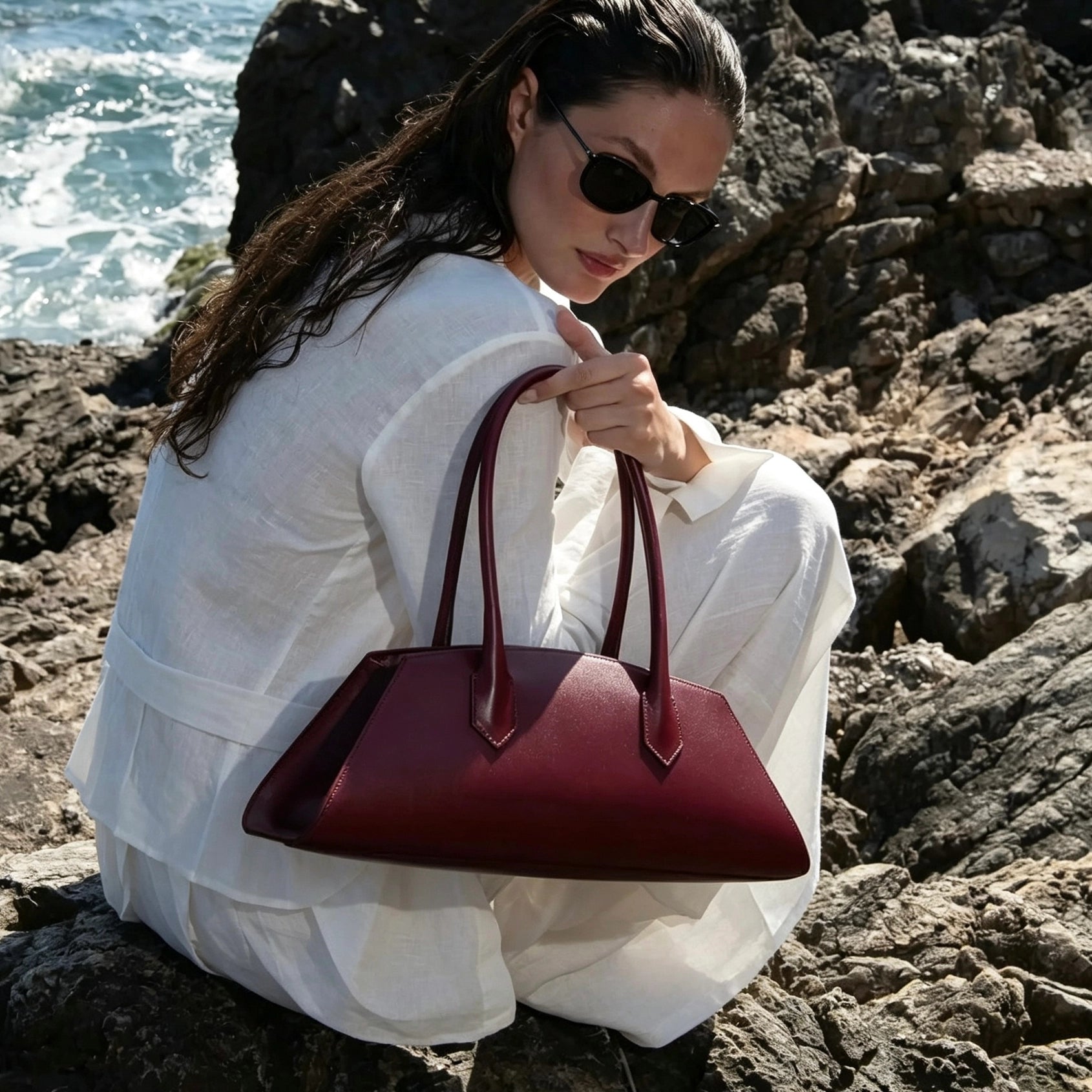 Model carrying the Nora Calfskin Shoulder Bag by Clemés in Burgundy, coastal setting