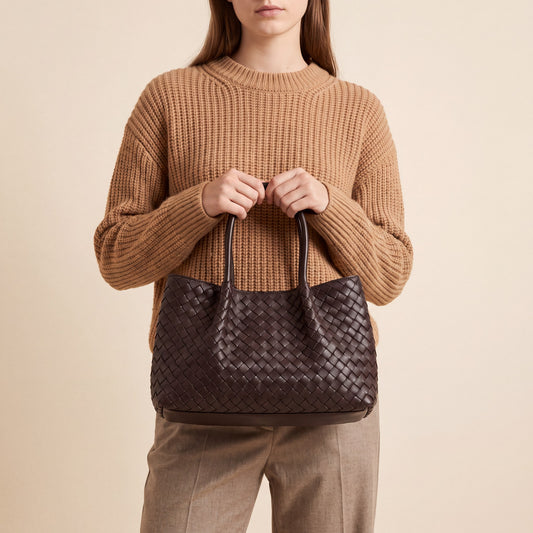 Model holding the Dark Brown Ornella woven leather bag by both top handles, studio shot
