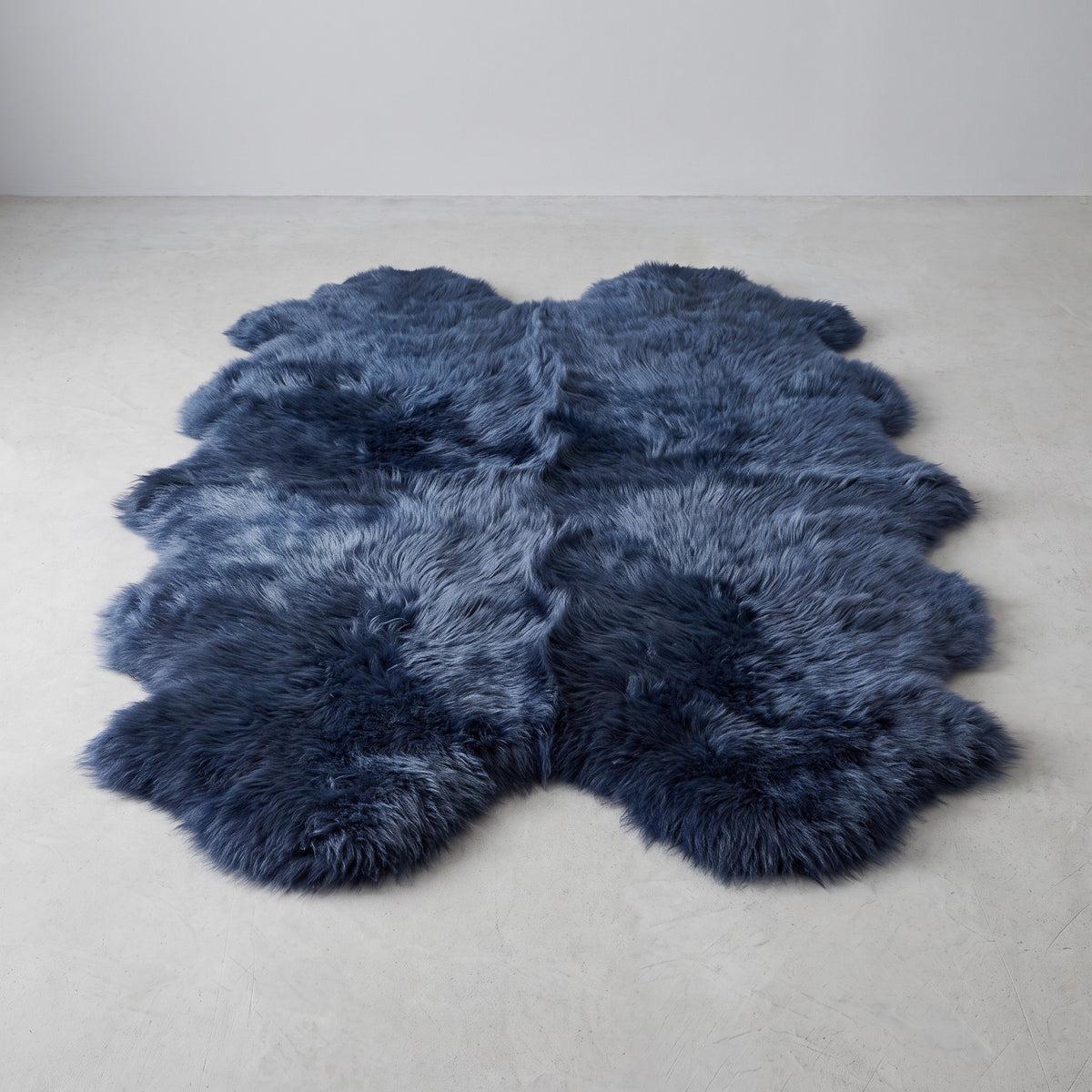 Indigo navy quad New Zealand sheepskin rug, L180 x W105 cm, on a pale grey studio floor