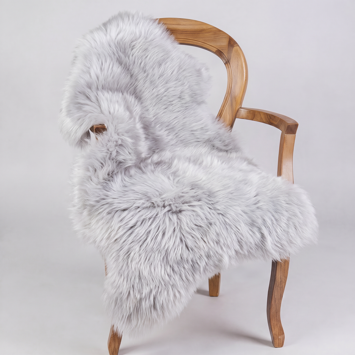 Silver sheepskin rug draped over a wooden armchair, front three-quarter view