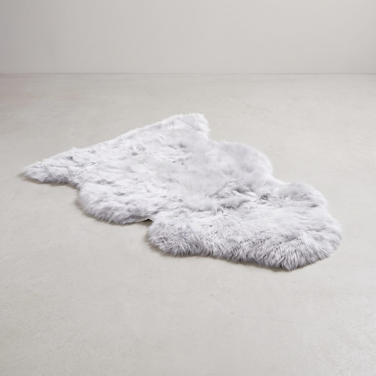 Silver single sheepskin rug laid flat on a pale grey floor