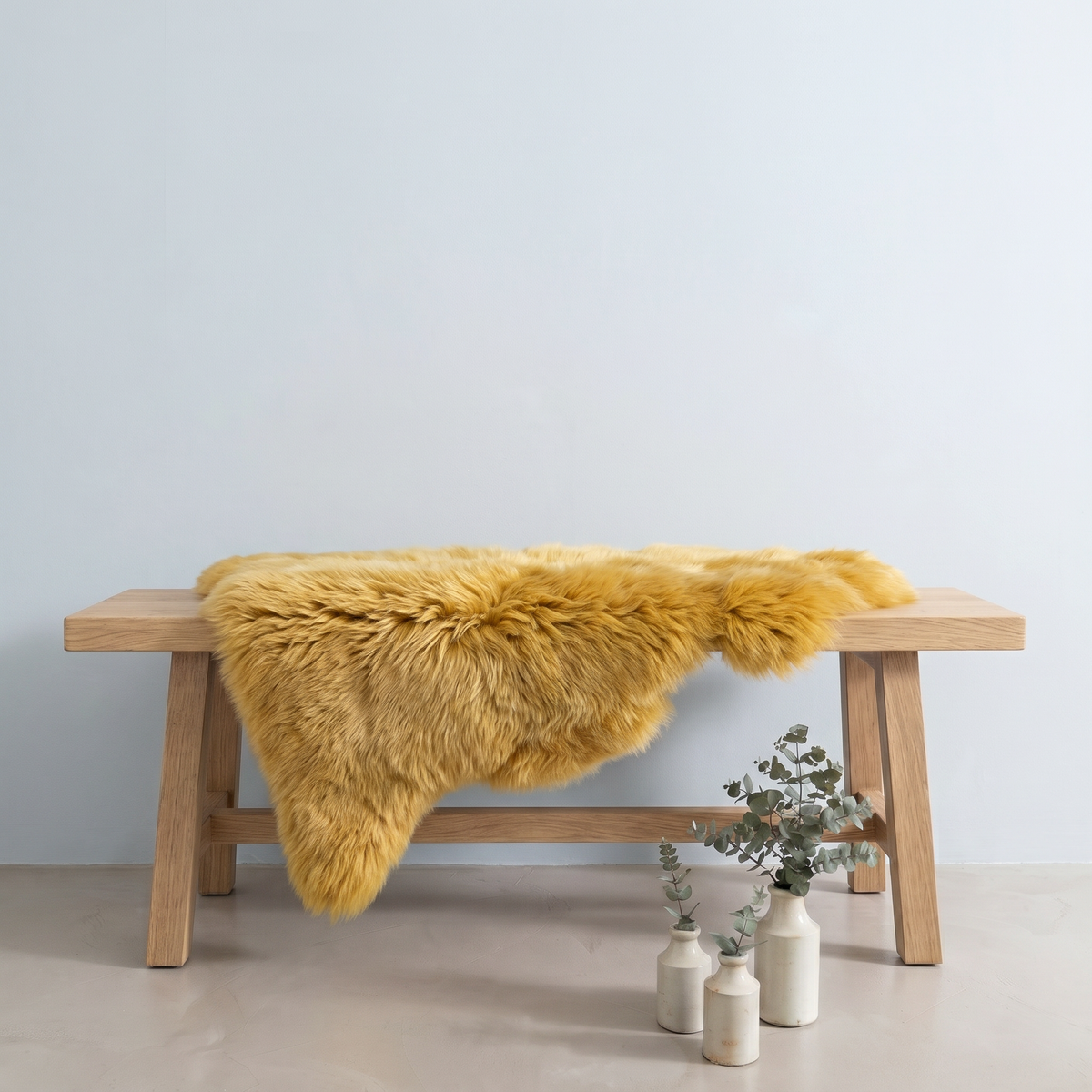 Squash sheepskin rug draped over an oak bench in a minimal interior