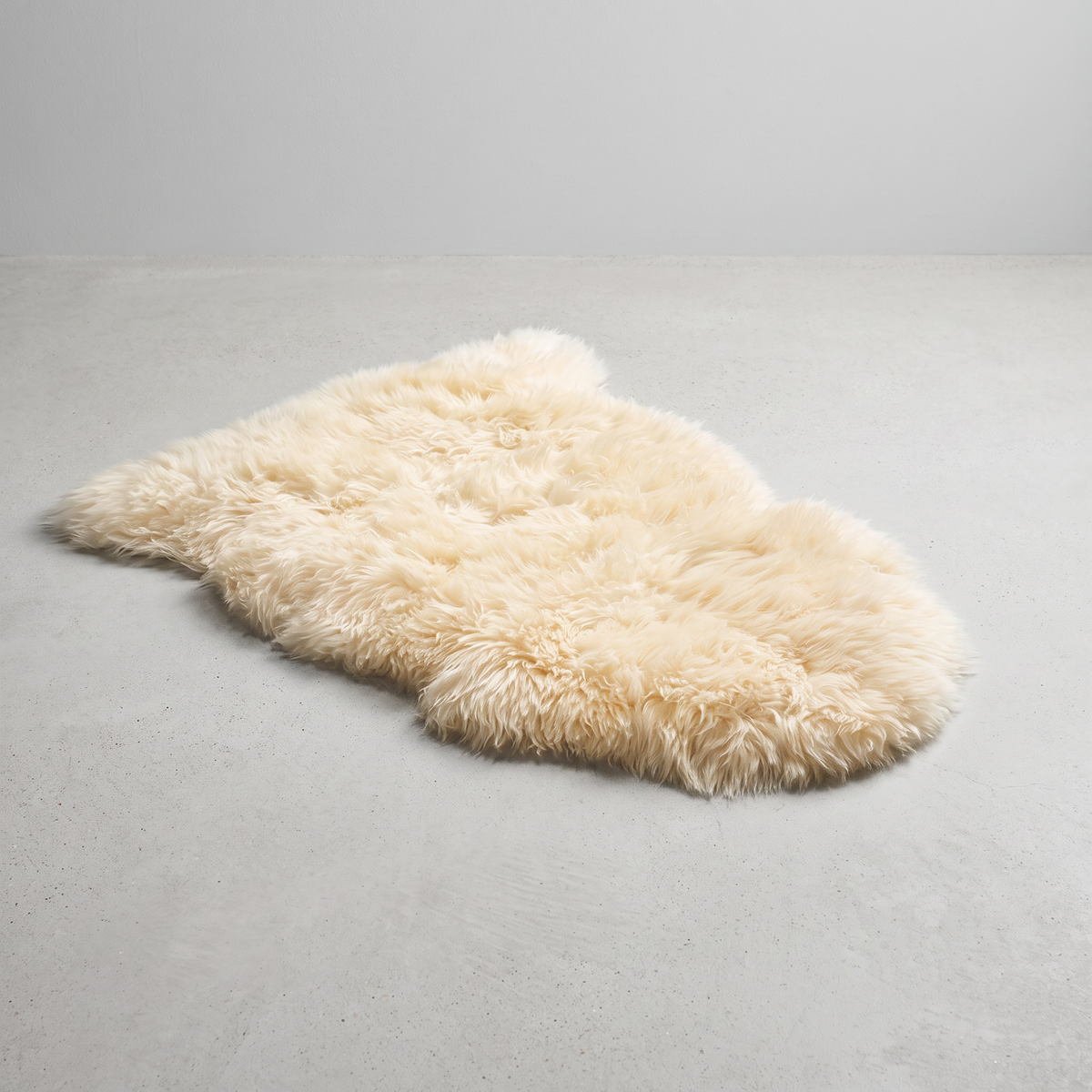 Champagne single sheepskin rug laid flat on a pale grey floor