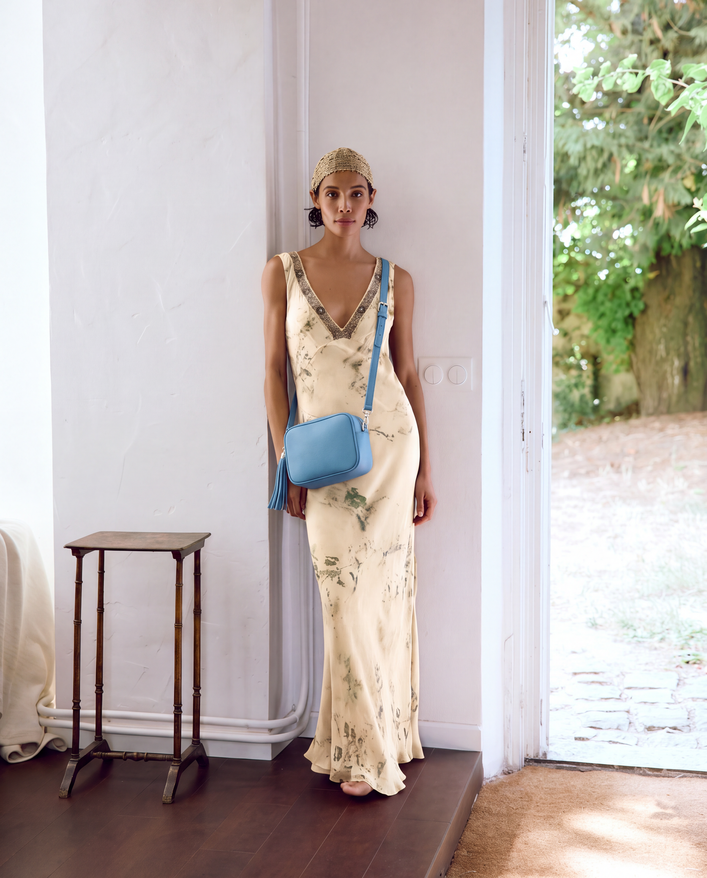 Model with the Sky Blue Éloise Leather Tassel Camera Bag by Clemés in a bright garden doorway