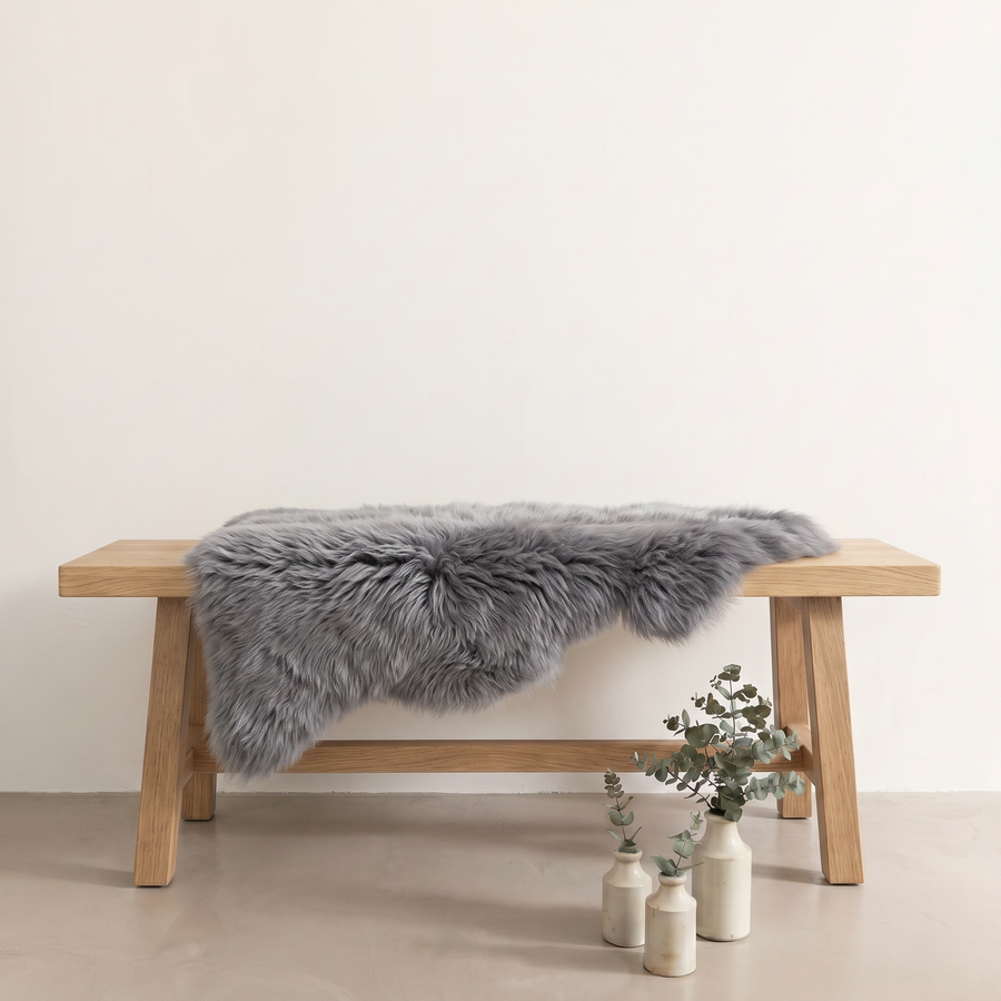 Grey sheepskin rug draped over an oak bench in a minimal interior