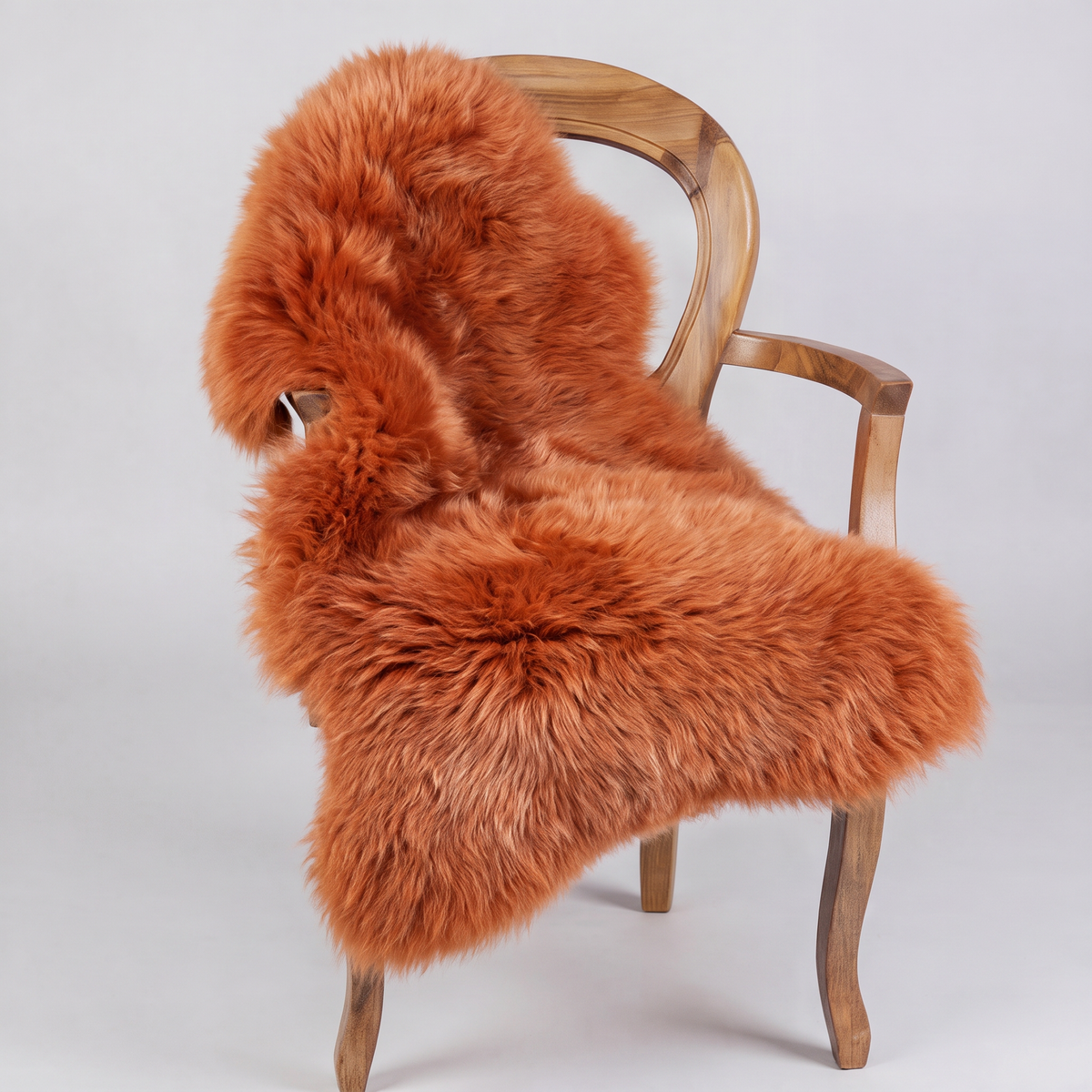 Burnt Orange single sheepskin rug draped over a wooden armchair, front three-quarter view