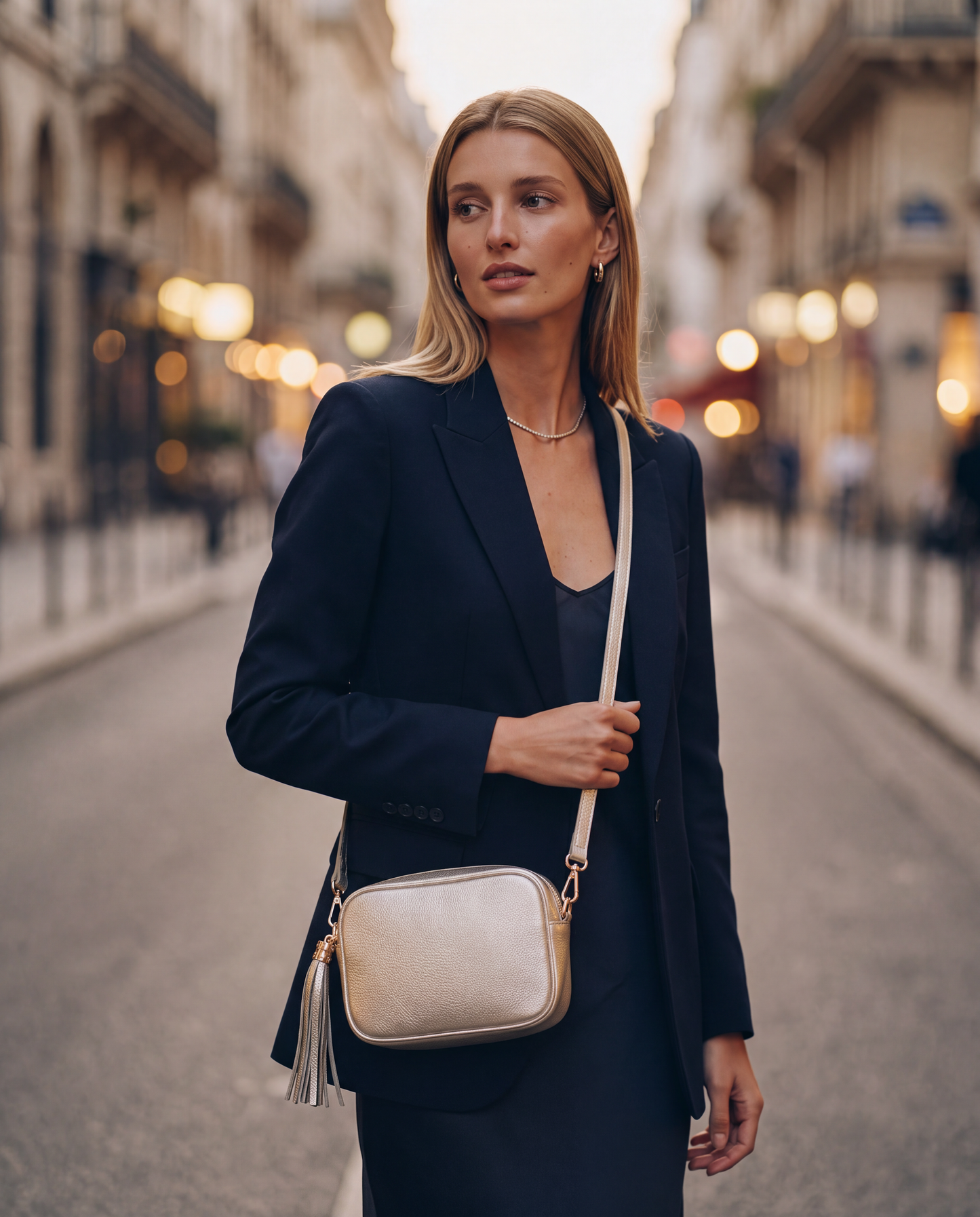 Model with the Metallic Gold Éloise Leather Tassel Camera Bag by Clemés on a city street at dusk