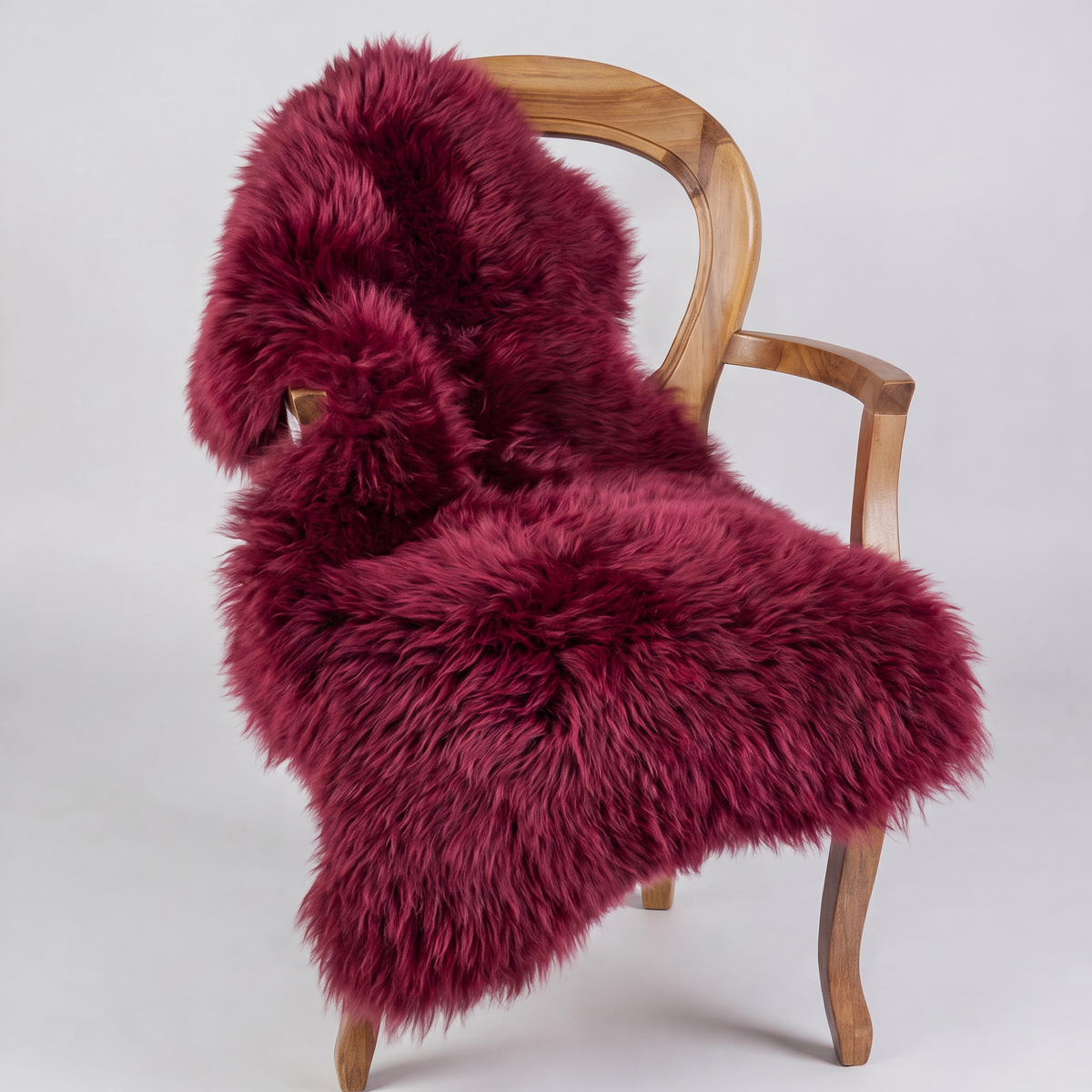 Raspberry sheepskin rug draped over a wooden armchair, front three-quarter view