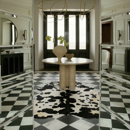 Black and white cowhide rug styled on the checkerboard marble floor of a monochrome mirrored entrance hall