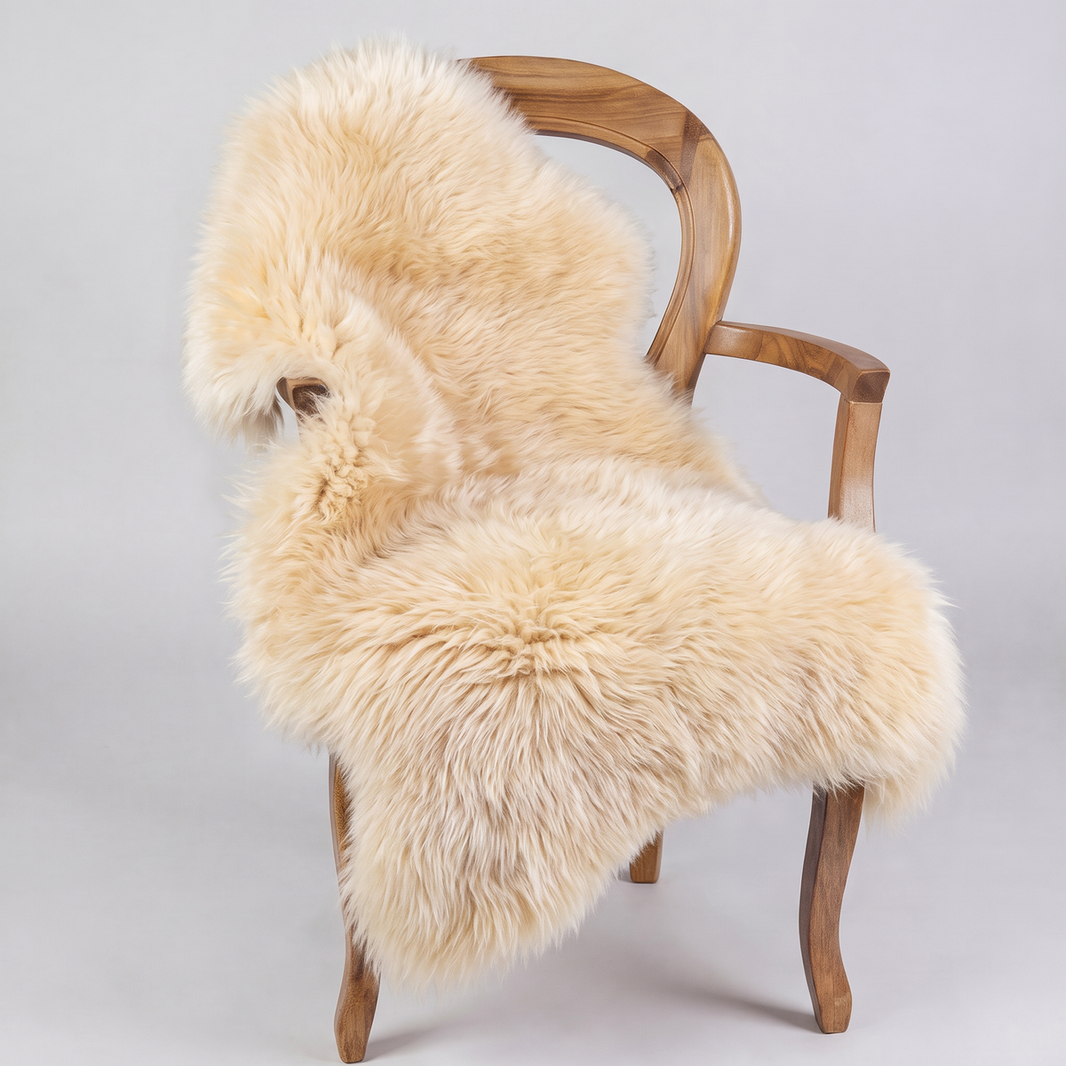 Champagne sheepskin rug draped over a wooden armchair, front three-quarter view