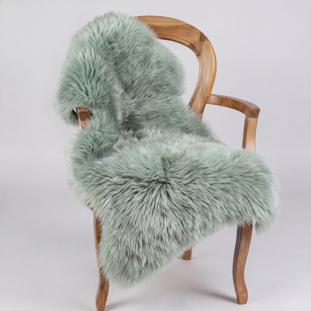 Sage green sheepskin rug draped over a wooden armchair, front three-quarter view