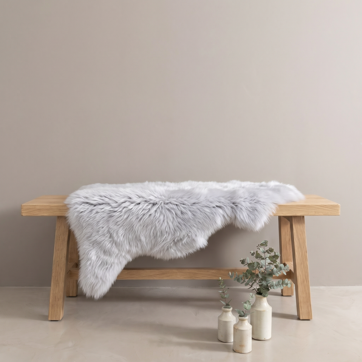 Silver sheepskin rug draped over an oak bench in a minimal interior
