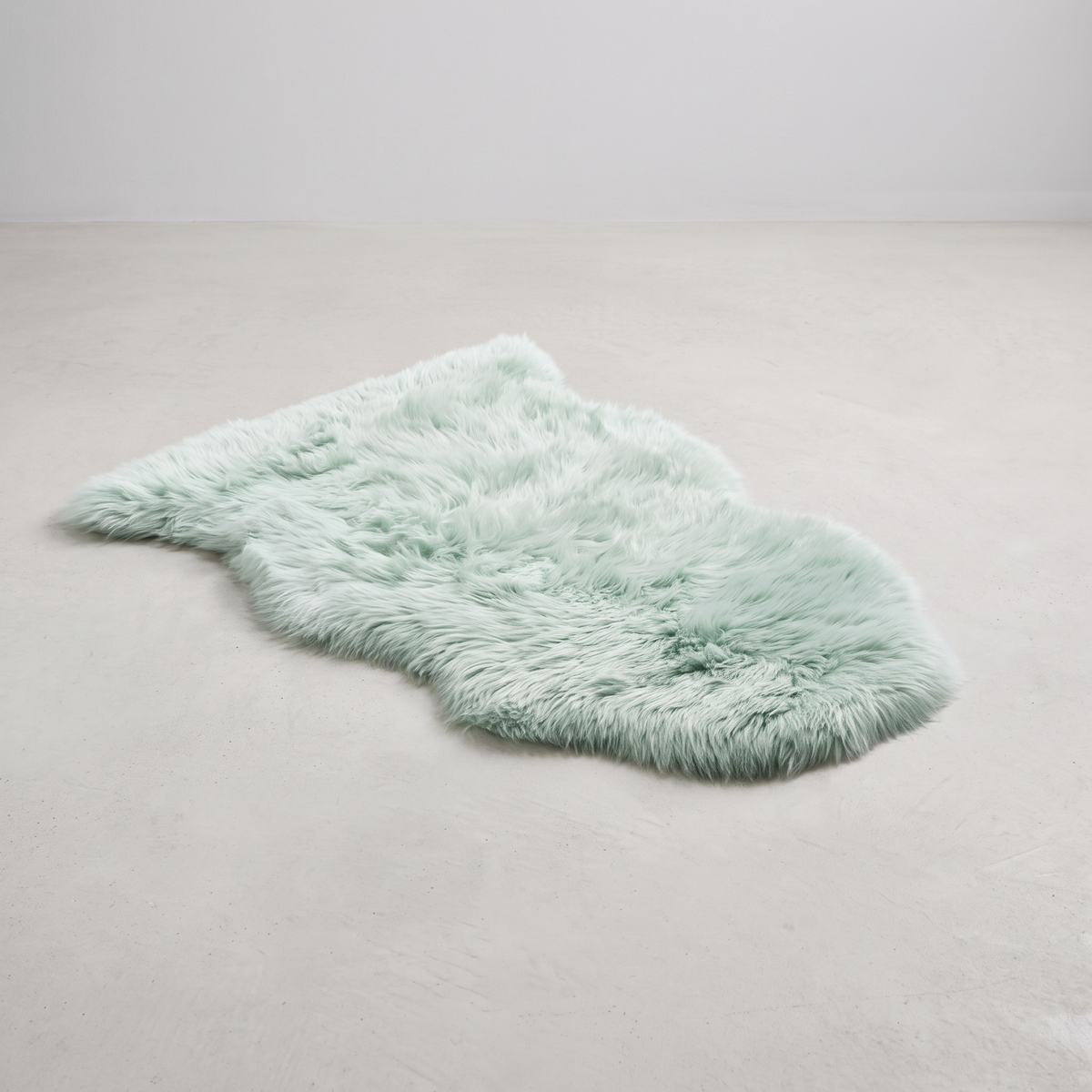 Sage green single sheepskin rug laid flat on a pale grey floor