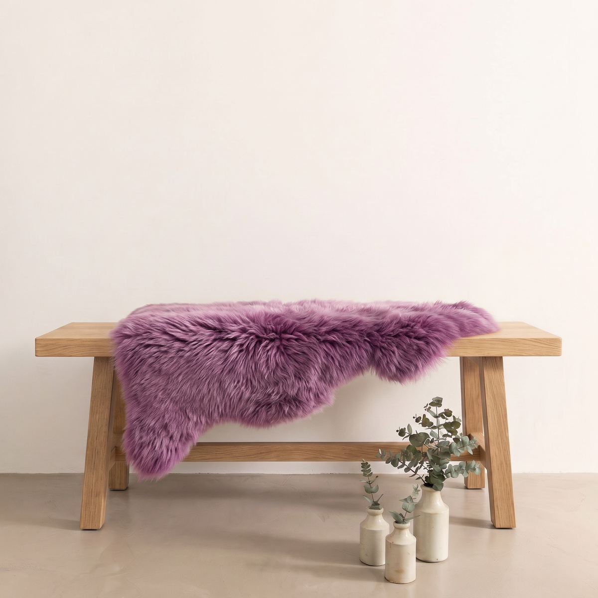 Medici purple sheepskin rug draped over an oak bench in a minimal interior