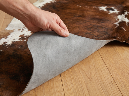 Natural grey suede back of cowhide rug shown by hand on light wooden floor
