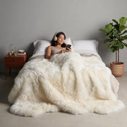 Ivory Octo New Zealand sheepskin rug throw styled on a bed, model relaxing with headphones