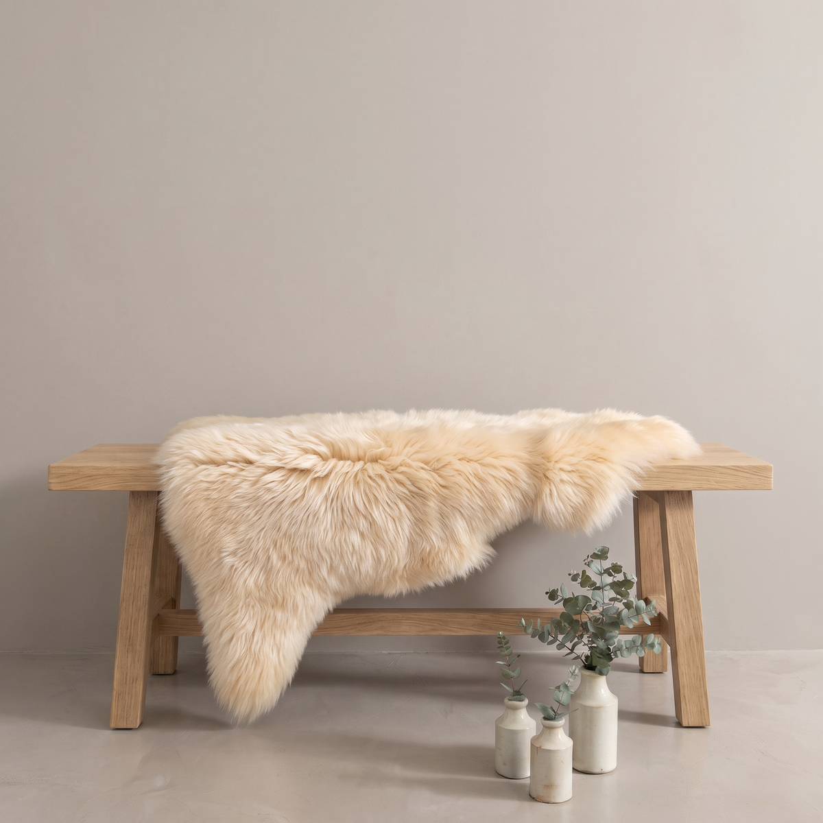 Champagne sheepskin rug draped over an oak bench in a minimal interior