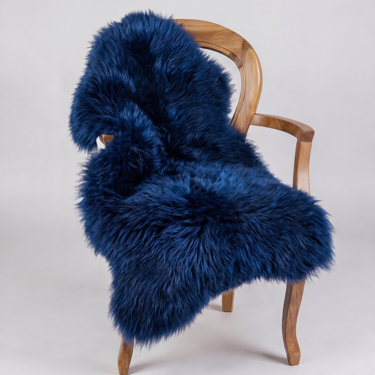 Cobalt Blue sheepskin rug draped over a wooden armchair, front three-quarter view