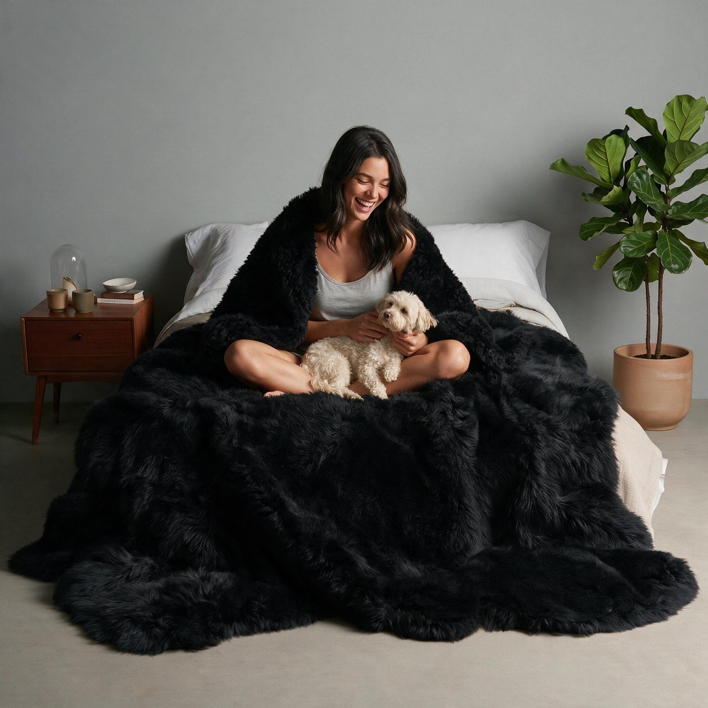 Black Octo New Zealand sheepskin rug throw styled on a bed, model with a small dog in her lap