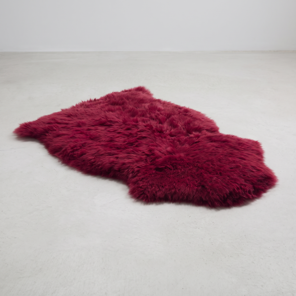 Raspberry single sheepskin rug laid flat on a pale grey floor