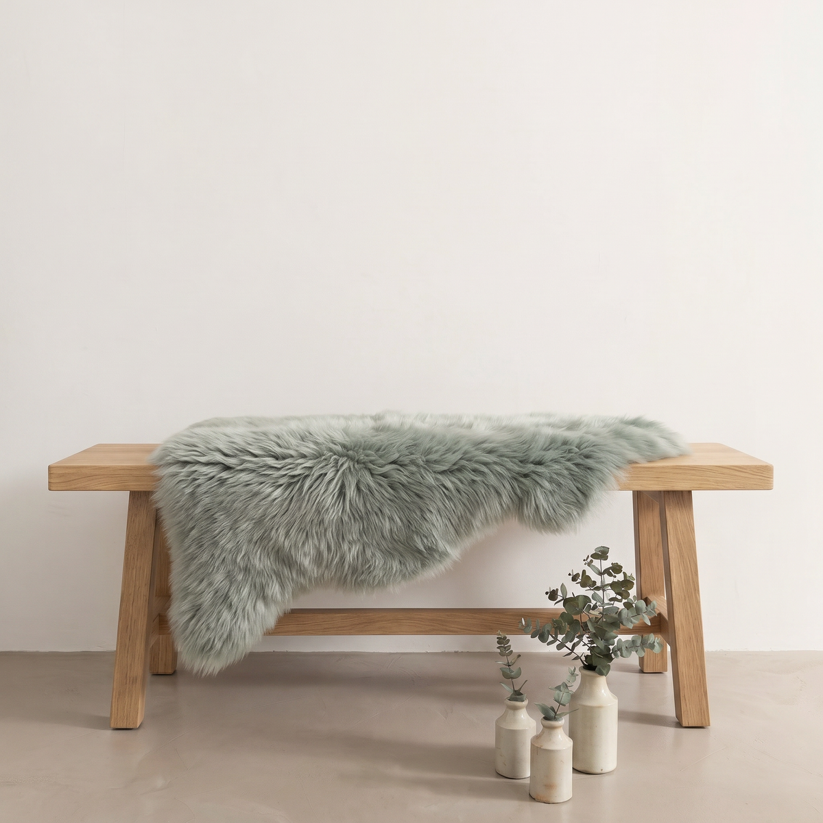 Sage green sheepskin rug draped over an oak bench in a minimal interior