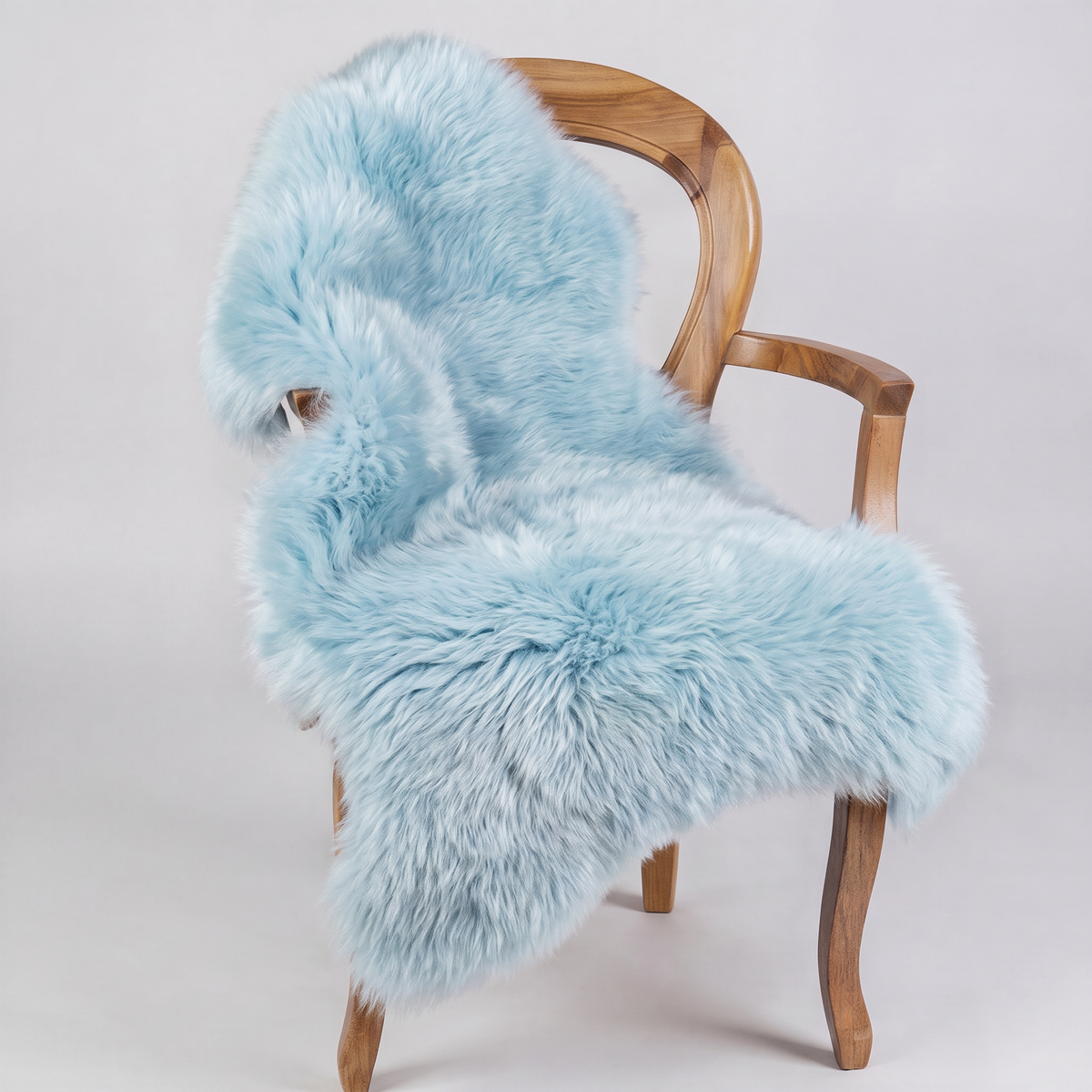 Sea Foam blue sheepskin rug draped over a wooden armchair, front three-quarter view