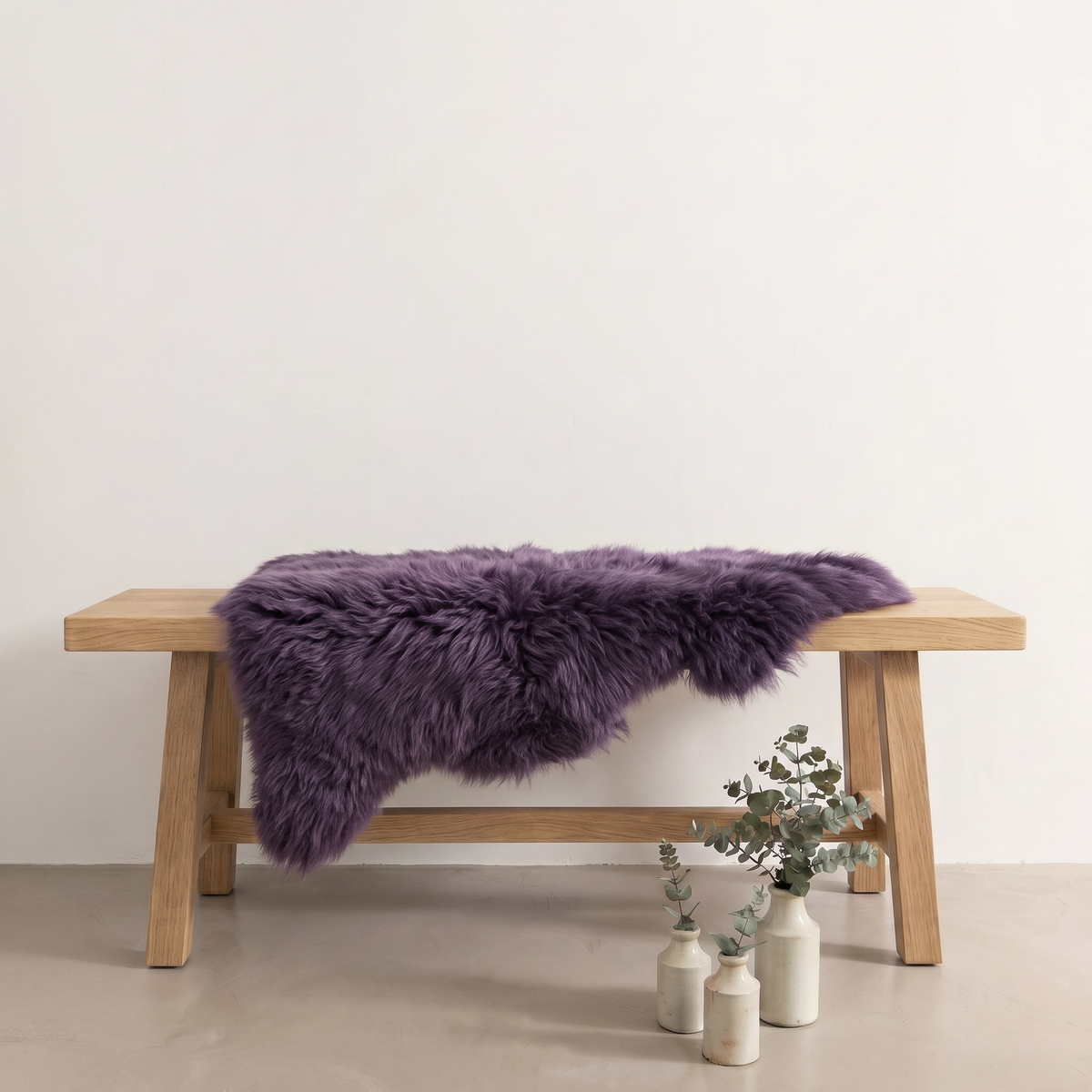 Purple sheepskin rug draped over an oak bench in a minimal interior