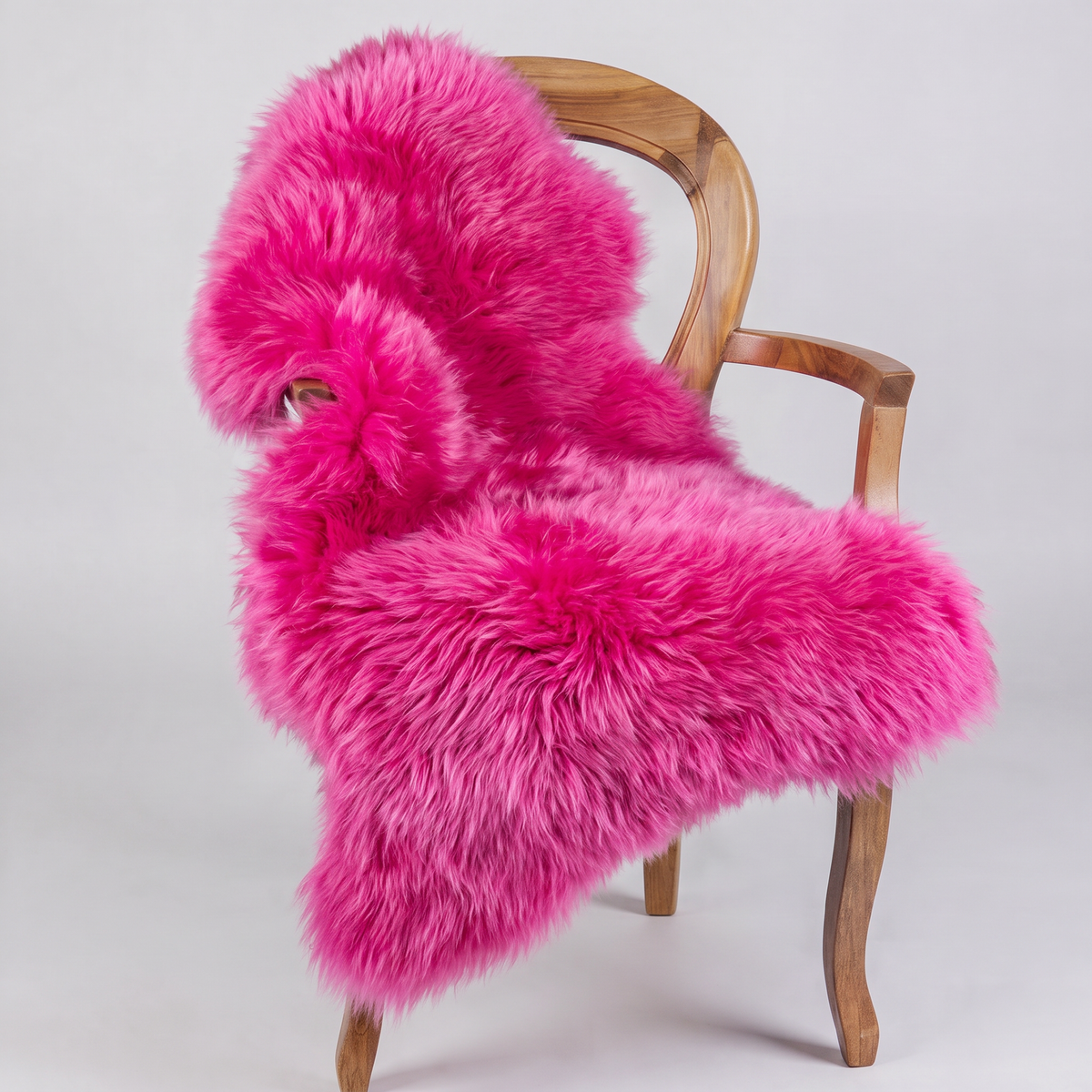 Fuchsia sheepskin rug draped over a wooden armchair, front three-quarter view