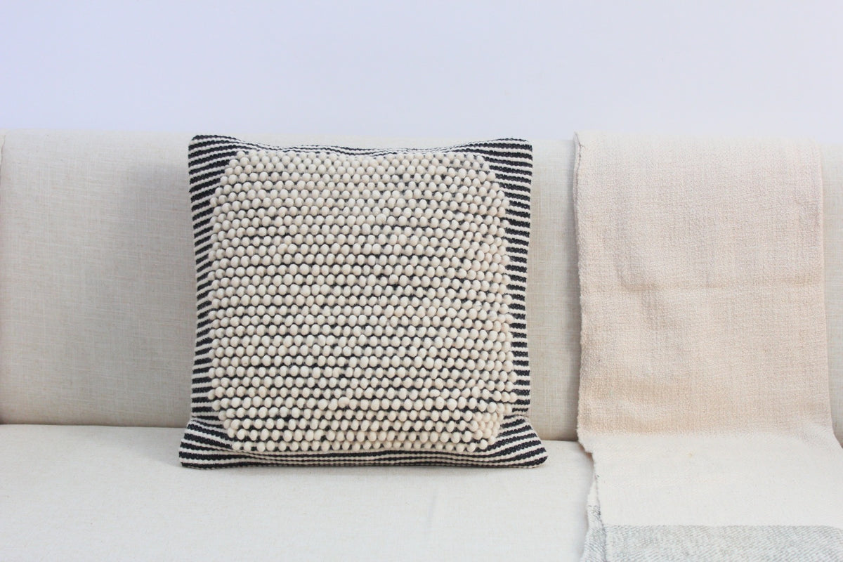 Salt & Pepper natural wool cushion cover, 50 x 50 cm, with an ivory bobble centre and black-and-white striped edges, on a cream sofa