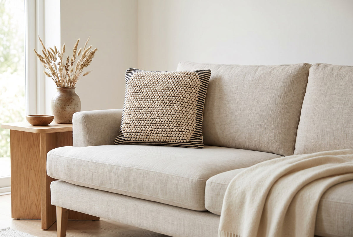 Salt & Pepper natural wool cushion cover styled on a pale linen sofa beside an oak side table, with a cream wool throw
