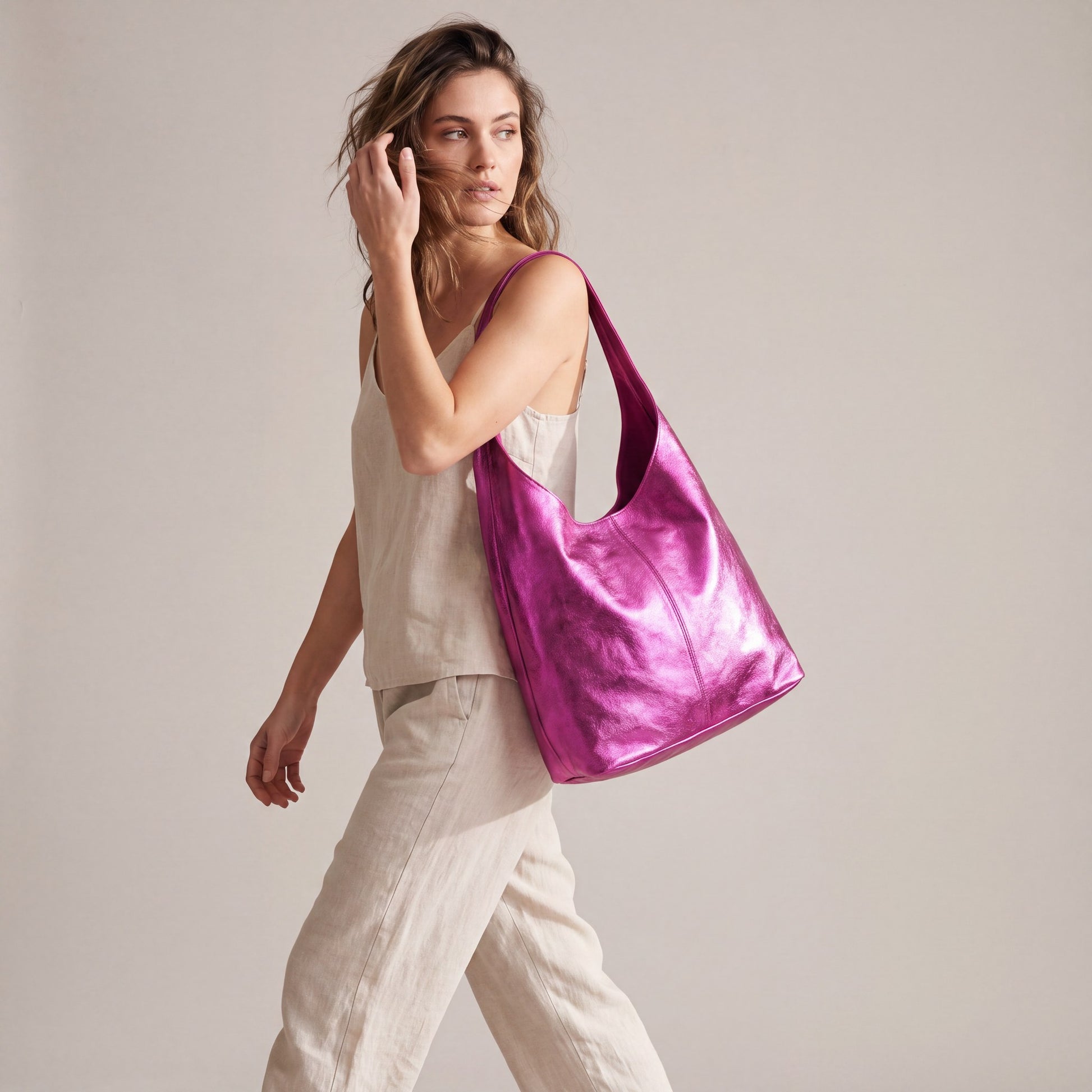Model walking with the Fuchsia Silvia Metallic Suede Slouch Bag on her shoulder, studio shot