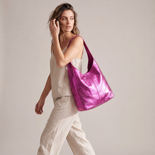 Model walking with the Fuchsia Silvia Metallic Suede Slouch Bag on her shoulder, studio shot