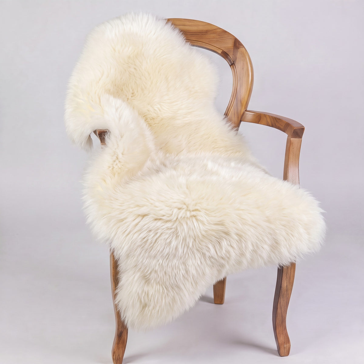 Ivory sheepskin rug draped over a wooden armchair, front three-quarter view