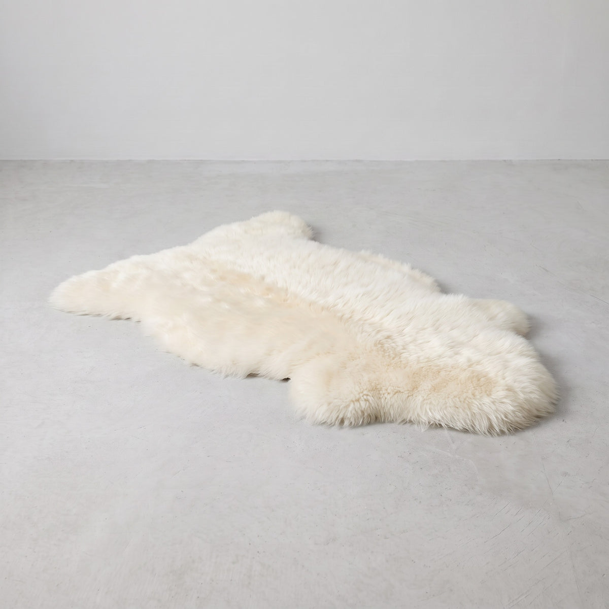 Ivory single sheepskin rug laid flat on a pale grey floor