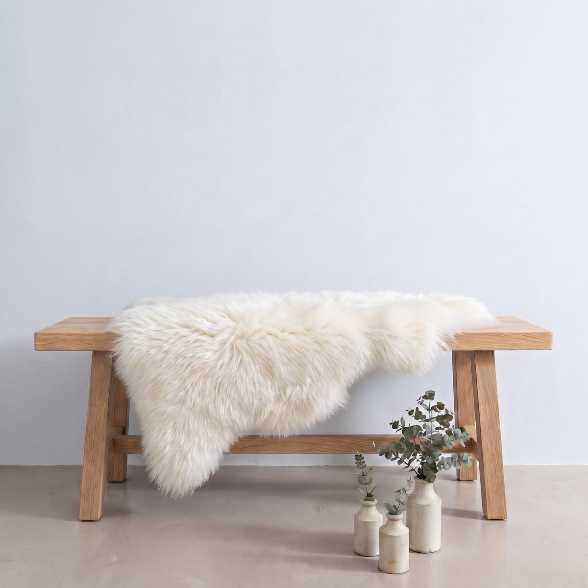 Ivory sheepskin rug draped over an oak bench in a minimal interior