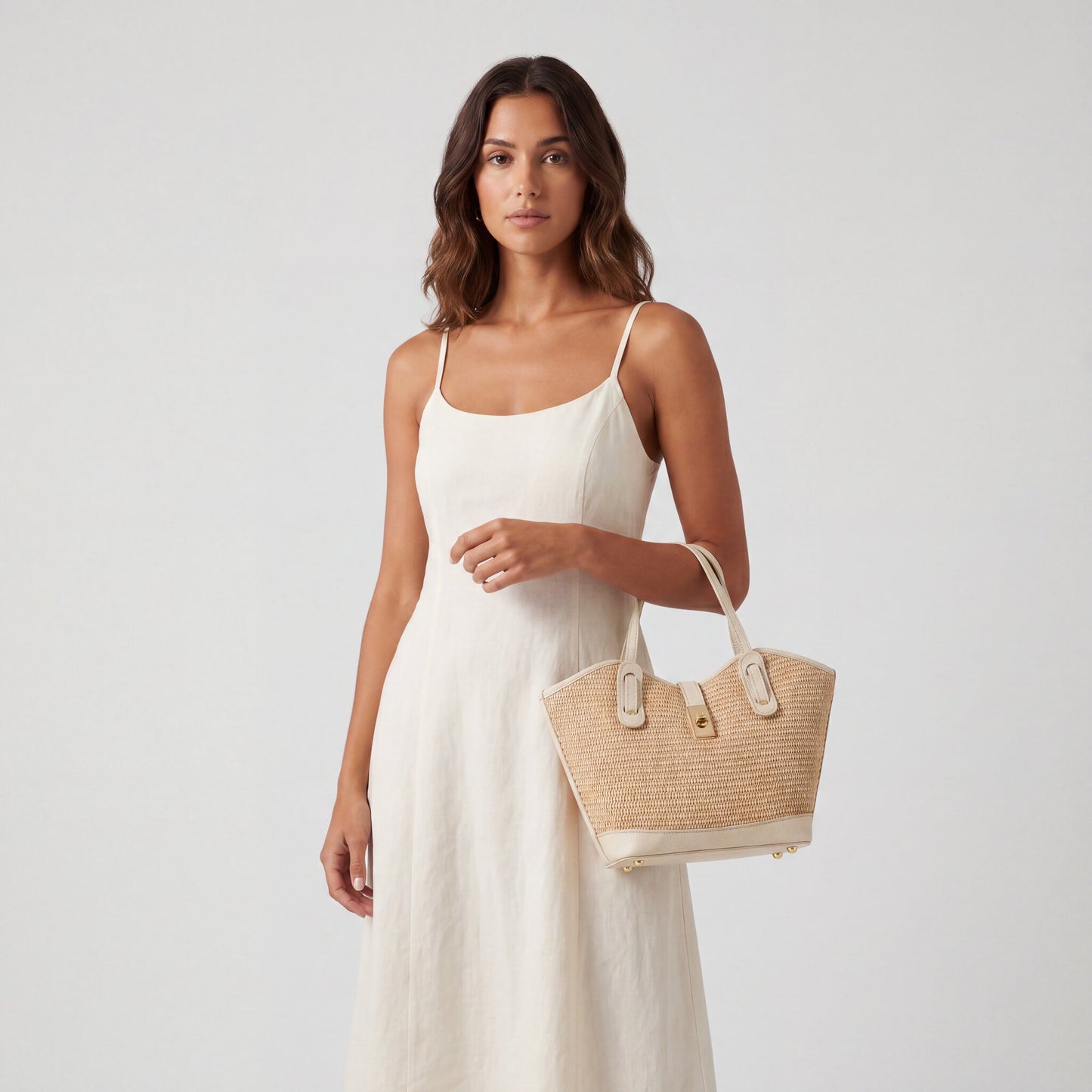 Model holding the Oyster Sorrento Raffia & Leather Tote by its top handles, arm at her side, studio shot