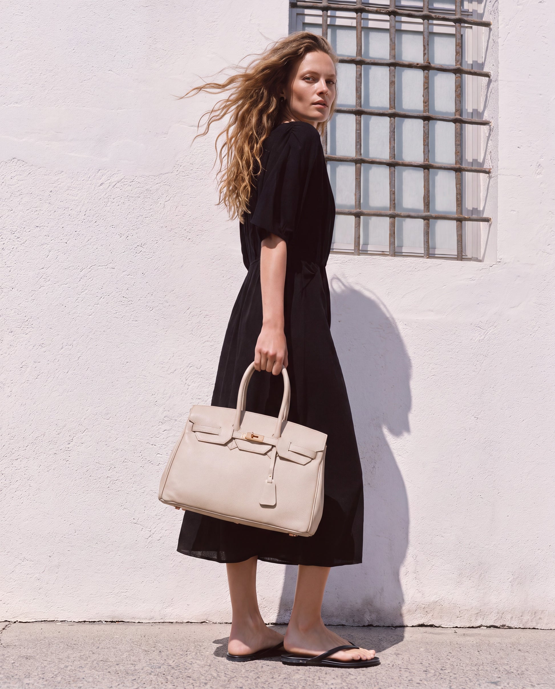 Woman by a whitewashed Mediterranean wall carrying the Oyster Valentina Maxi Leather Tote