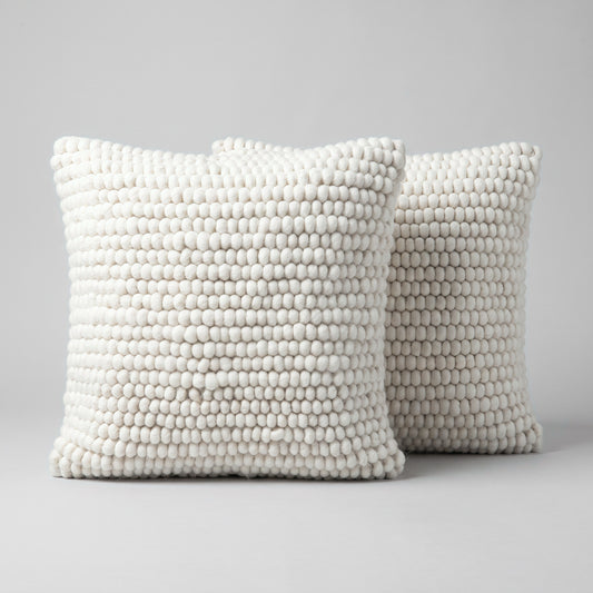 Pair of natural ivory wool cushion covers, 50 x 50 cm, with hand-felted wool balls, on a light grey studio background