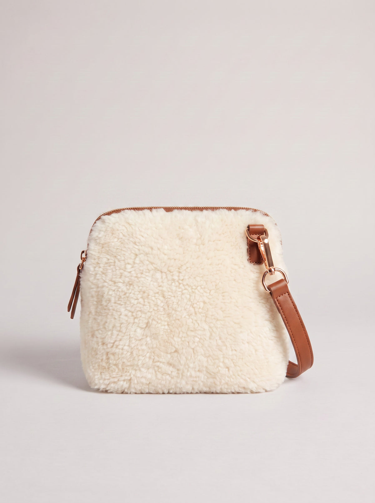 Zita faux shearling crossbody bag in ivory with brown leather strap, on a light grey studio background