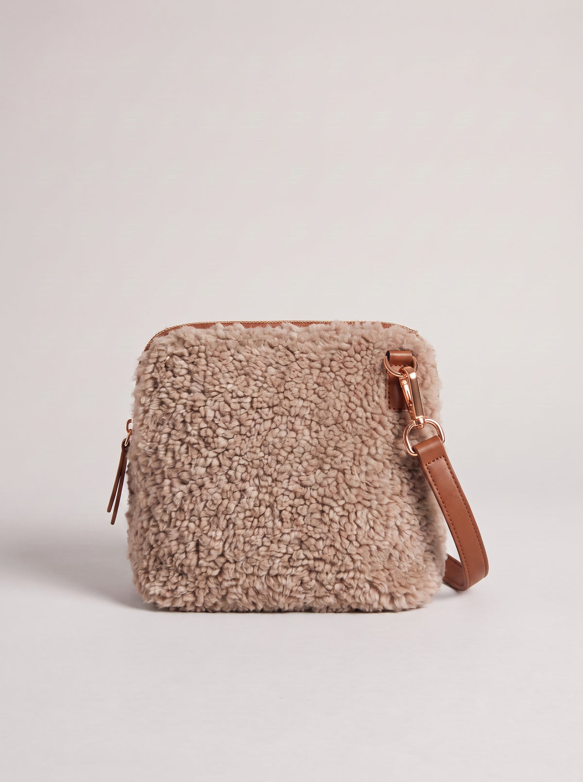 Zita faux shearling crossbody bag in light taupe with brown leather strap, on a light grey studio background